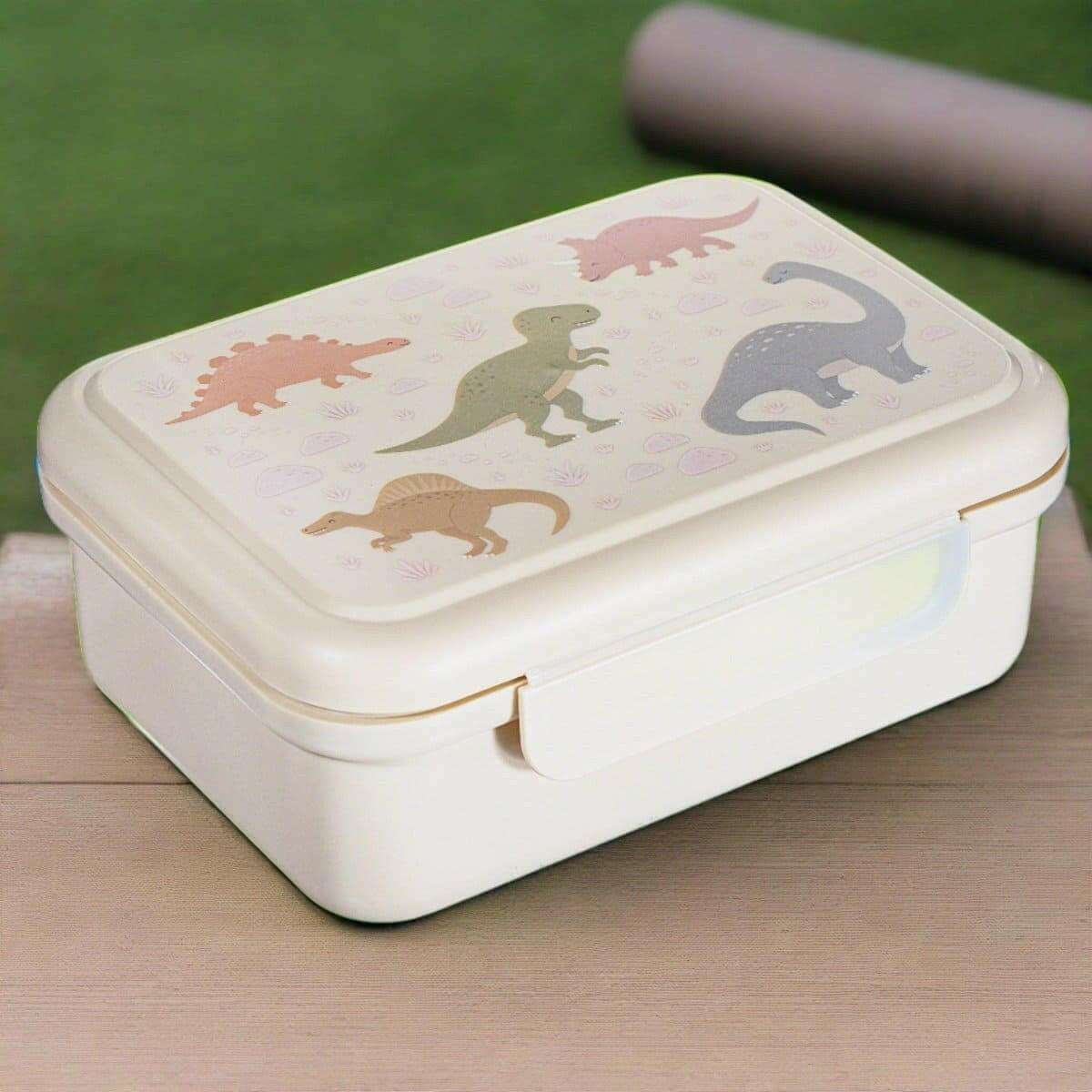 Cream kids lunch box with dinosaur graphic lid, side clasp closed on table