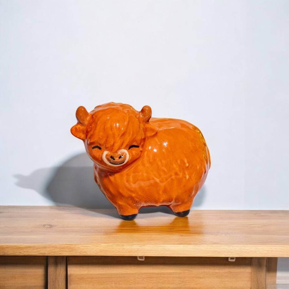 Glossy orange Highland cow figurine on a wooden shelf, full body profile