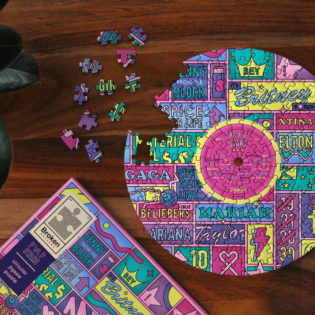 LP-shaped jigsaw puzzle with scattered pieces and box featuring colorful pop-star collage