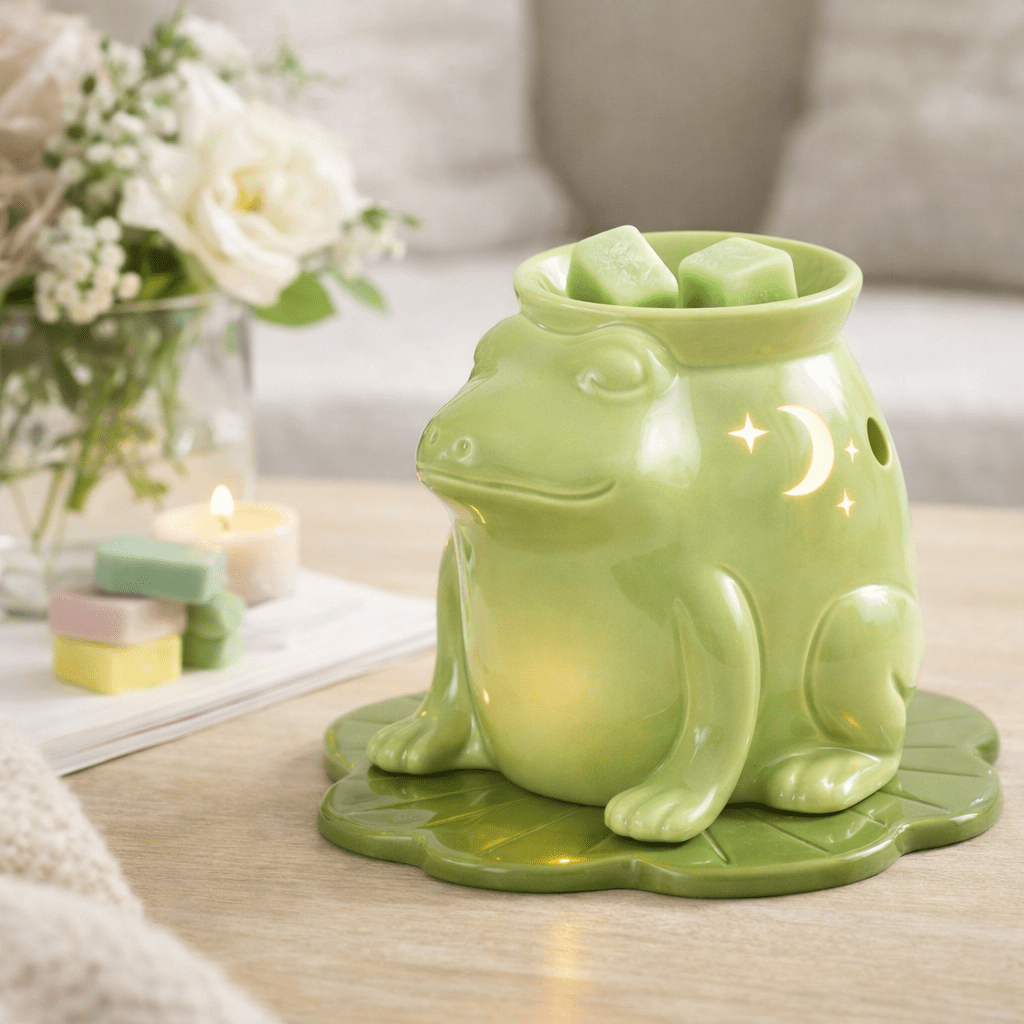 Green frog-shaped wax warmer on a table with candles and flowers in the background