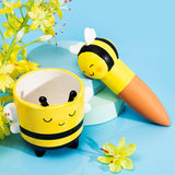 Bee-themed planter and carrot-shaped container with a bee design on a blue background with yellow flowers.