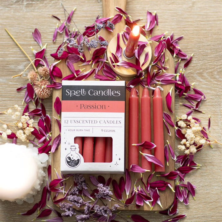 Open Spell candles carton with red unscented candles, lit wicks and purple petals