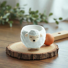 Sheep-shaped ceramic egg cup with facing sheep face, holding a brown egg