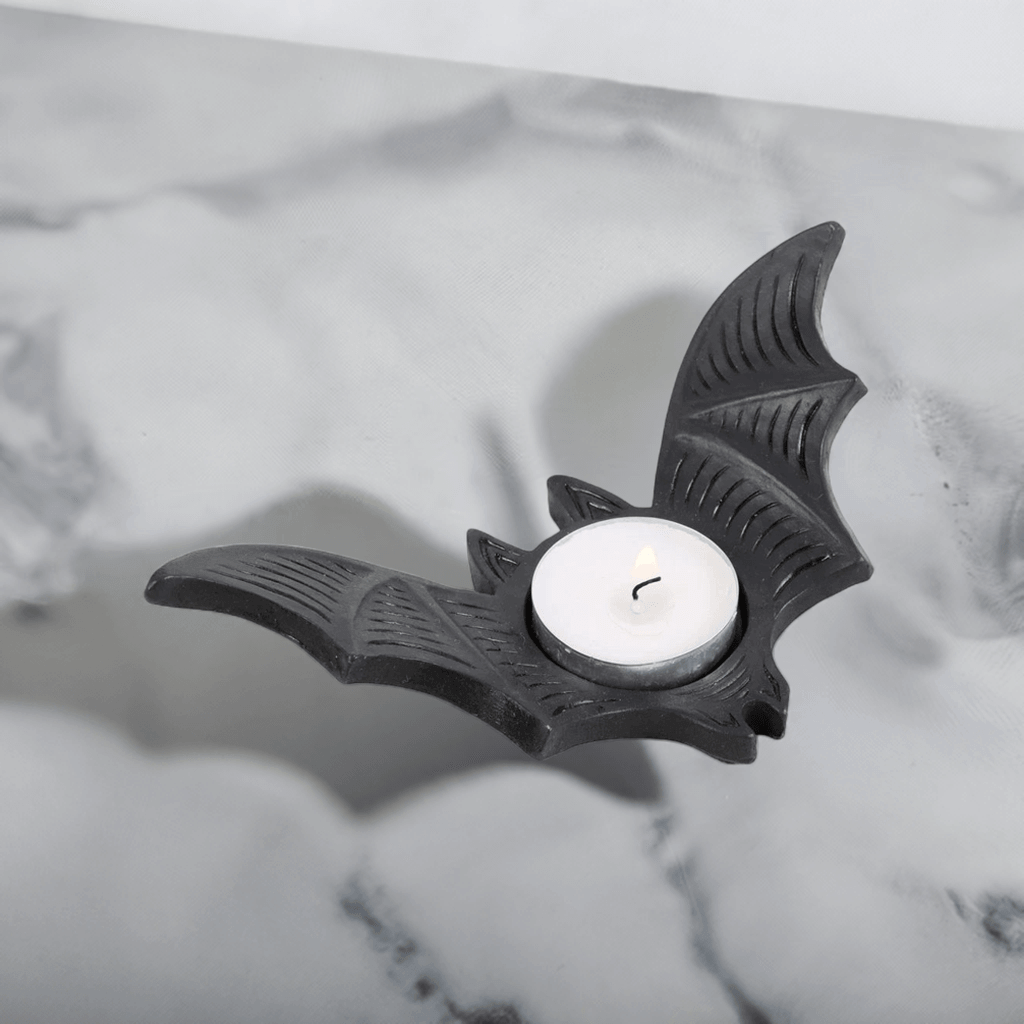 Bat-shaped tealight candle holder with lit white candle in round recess, black.