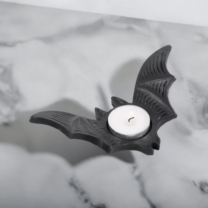 Bat-shaped tealight candle holder with lit white candle in round recess, black.