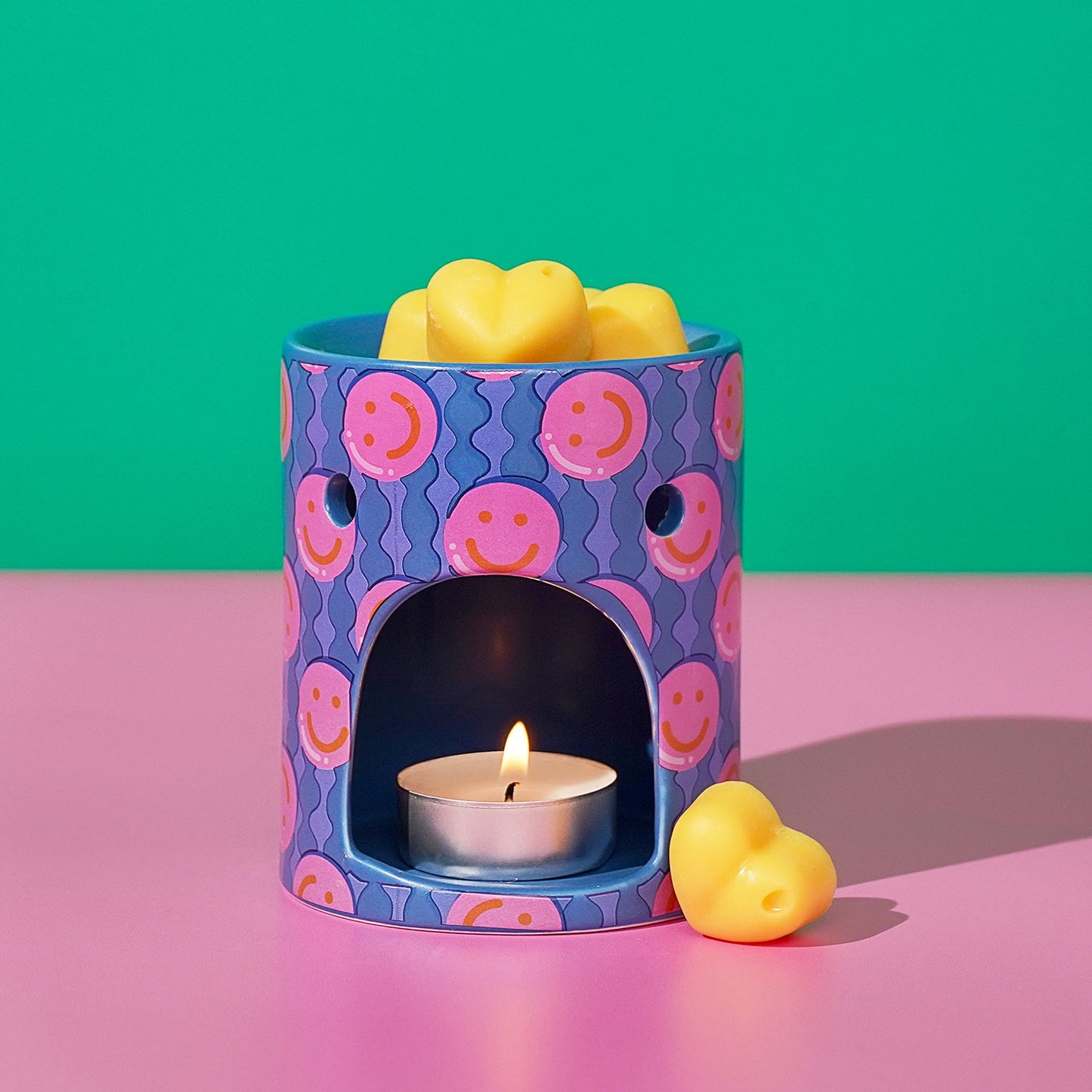 Purple patterned wax melt burner with lit tea light and yellow wax melt.