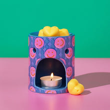 Purple patterned wax melt burner with lit tea light and yellow wax melt.