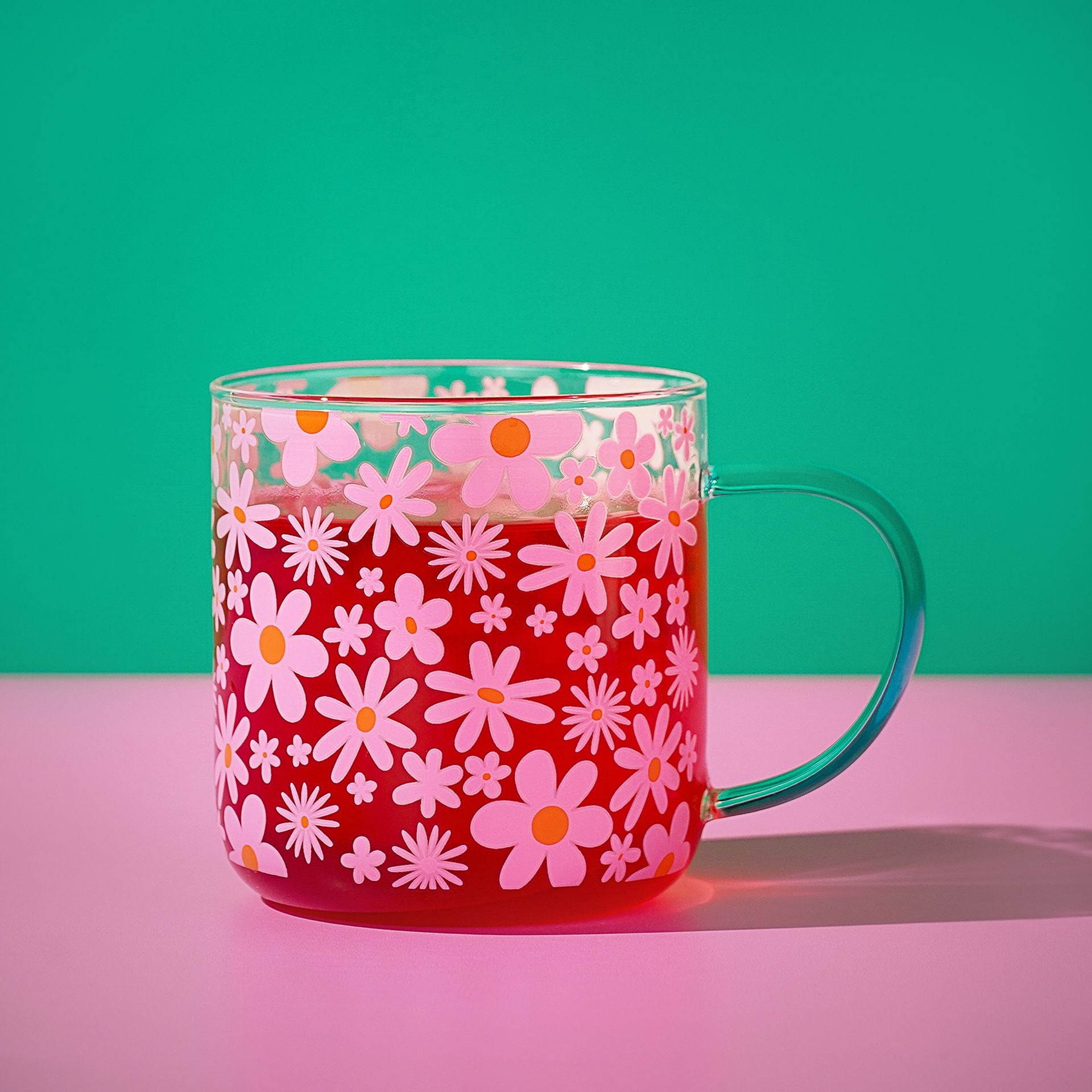 Pink floral glass mug with orange and white daisies; mint green curved handle.