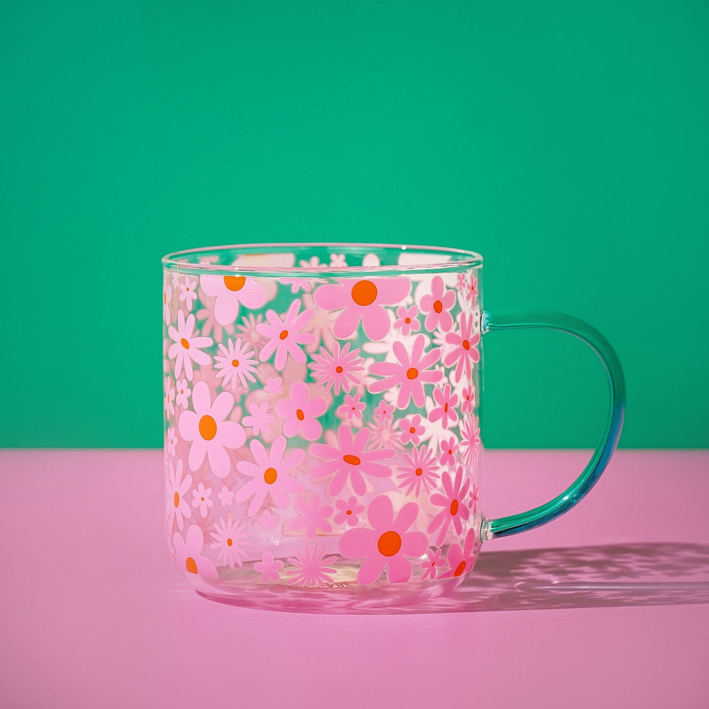 Pink floral glass mug with orange and white blossoms; mint green handle and clear rim.