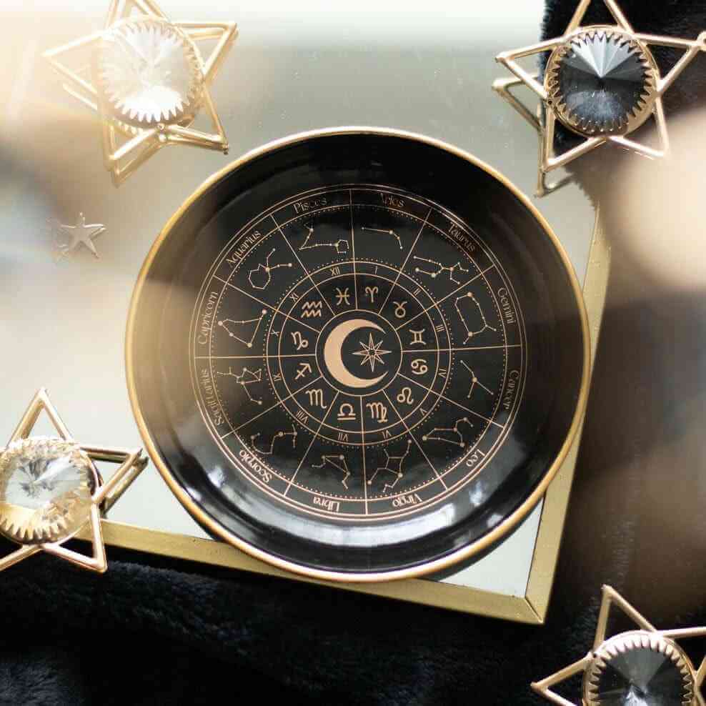 Black astrology trinket dish with gold rim and zodiac symbols in a circular layout
