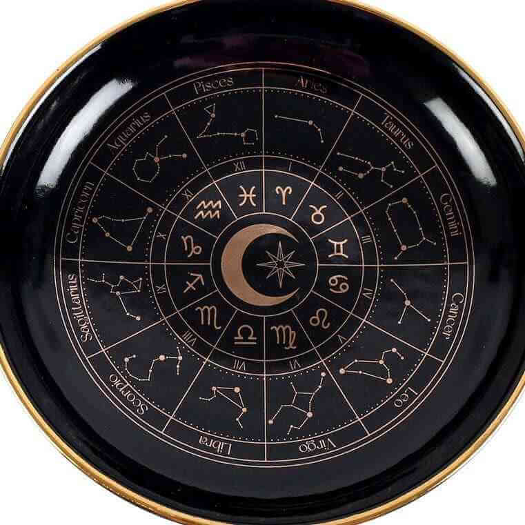 Close-up of black astrology wheel dish with gold rim and detailed zodiac ring
