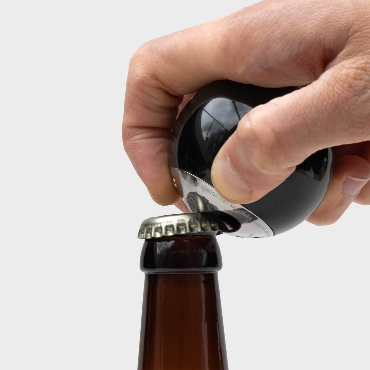 Black 8-ball bottle opener in use, hands lifting opener from a beer bottle