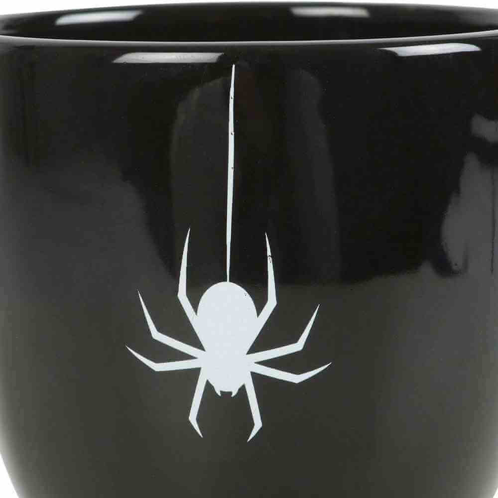 Close-up of white spider web and spider emblem on glossy black teacup