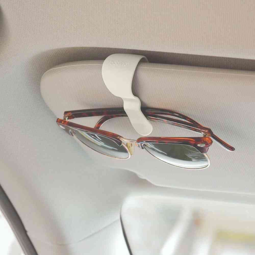 Cream glasses clip with C-shaped cradle holding eyeglasses on a car surface
