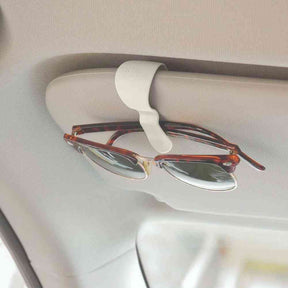 Cream glasses clip with C-shaped cradle holding eyeglasses on a car surface