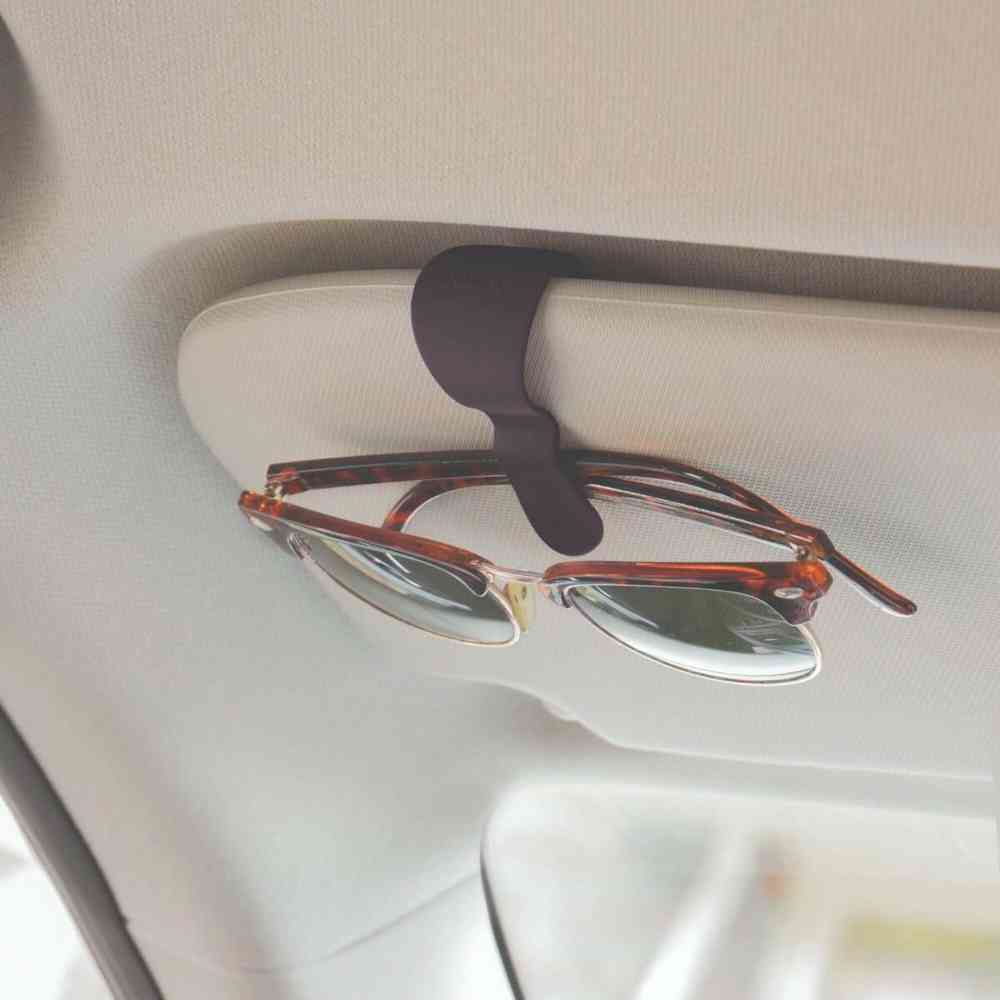 Black glasses clip with C-shaped cradle holding eyeglasses on a car surface