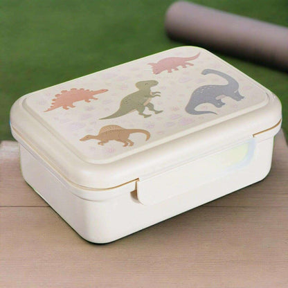Cream kids lunch box with dinosaur graphic lid, side clasp closed on table