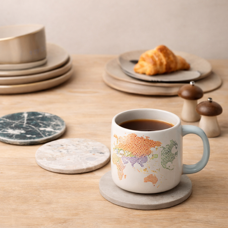 Mug with world map design on a wooden table with croissant and plates.