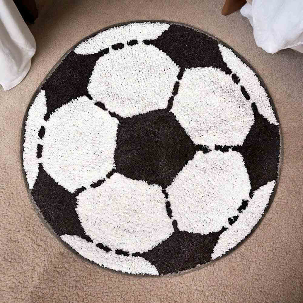 Round football-shaped rug featuring white soccer balls on a dark background with dashed seams.