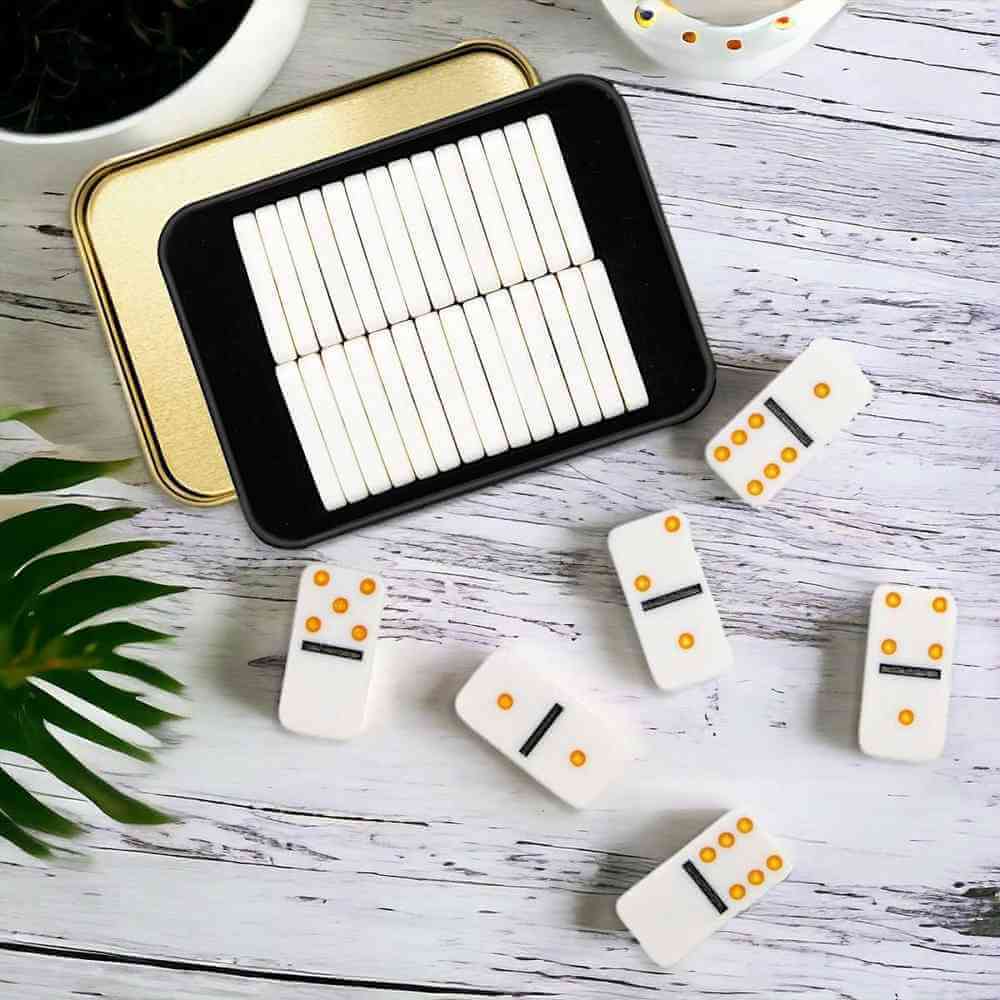 Pocket domino tin with open tray and white domino tiles scattered around it