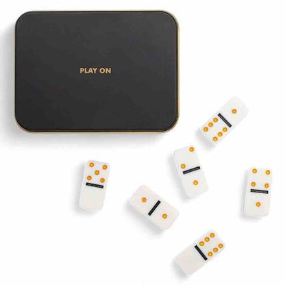 Black pocket domino tin with gold trim and white domino tiles scattered below