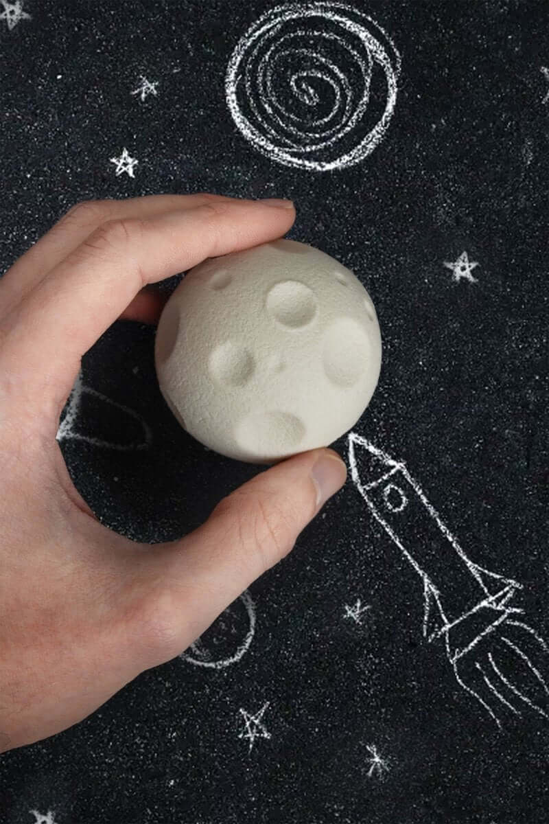 Hands holding cream moon-shaped rubber eraser on dark star-patterned surface