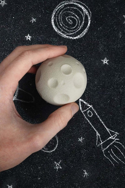 Hands holding cream moon-shaped rubber eraser on dark star-patterned surface