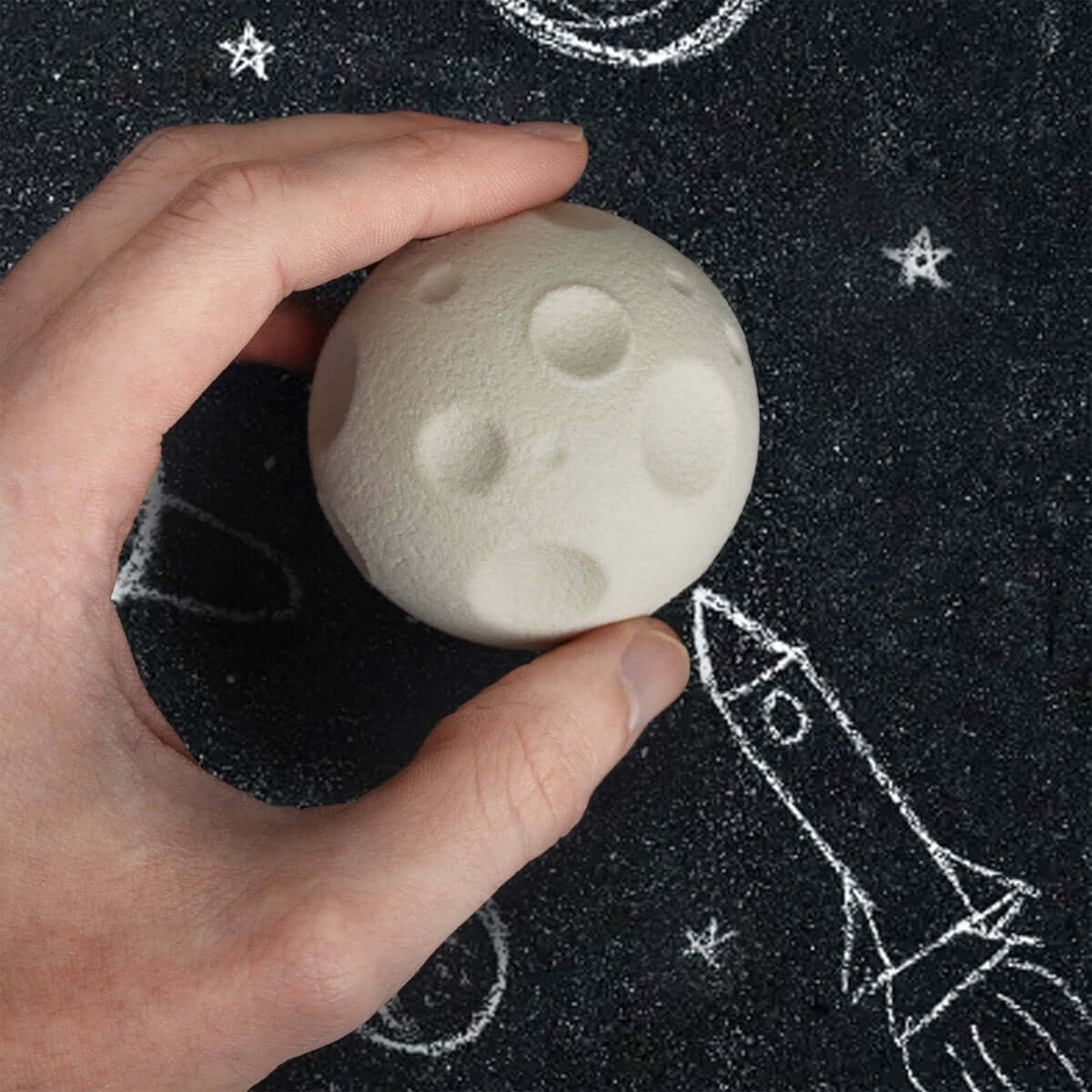 Hand holding cream moon-shaped rubber eraser with crater-like embossed details