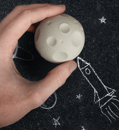 Moon-shaped rubber eraser, cream color with raised crater details, held in hand