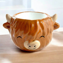 Brown ceramic cow egg cup with smiling face, small horns, and open top
