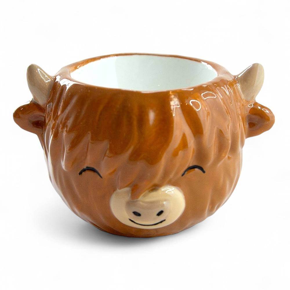 Brown glazed ceramic egg cup shaped like a cow with closed eyes and open top