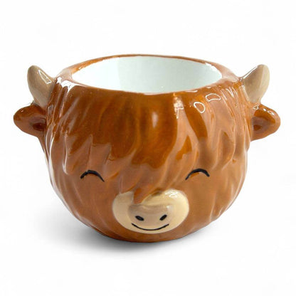Brown glazed ceramic egg cup shaped like a cow with closed eyes and open top