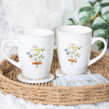 Two white ceramic mugs with bouquet-in-pot print and pink rims with floral coasters