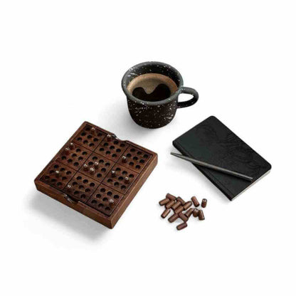 Wooden Sudoku puzzle board with black booklet, cup, and wooden peg pieces