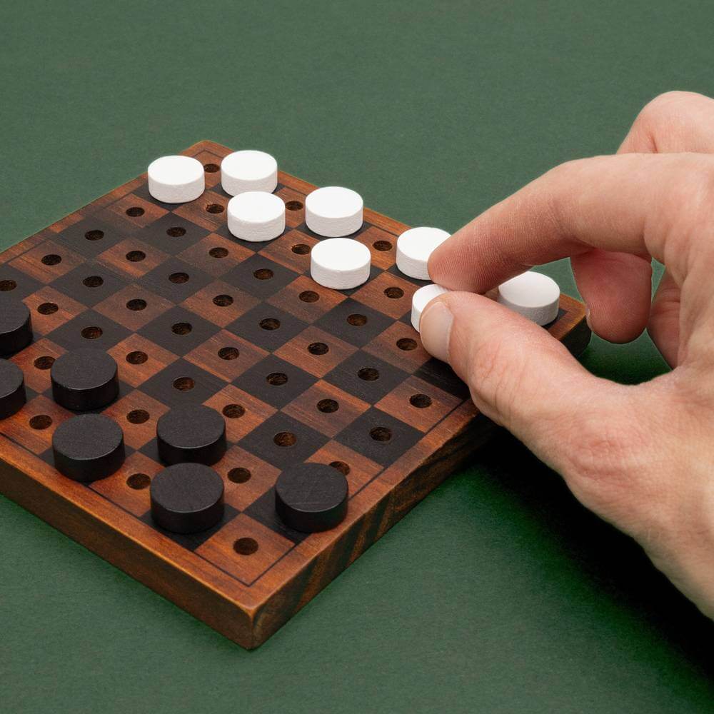 Wooden chess and checkers game board with dark and light round pieces; hand moving a piece