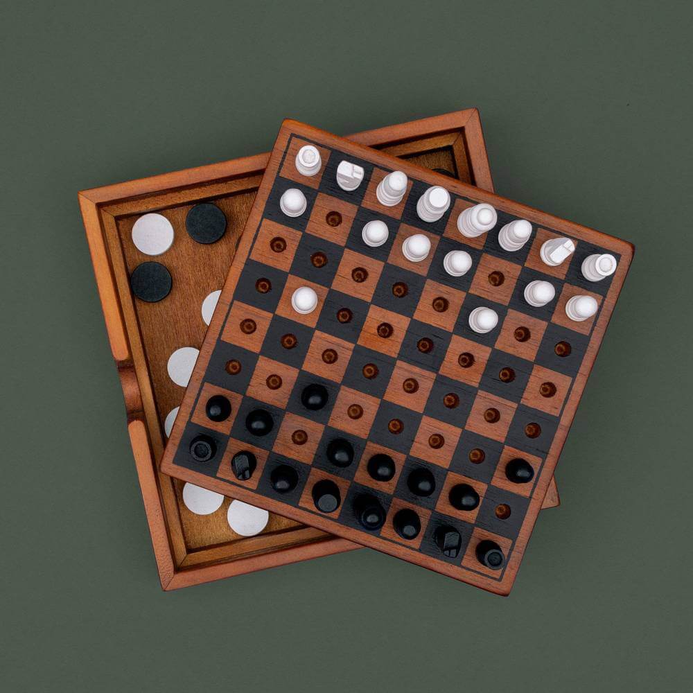 Wooden chess and checkers set with two boards stacked, dark and white pieces on squares