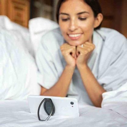 Black phone holder stand holding a phone on a bed for hands-free viewing