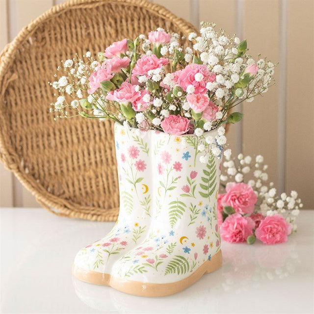 Floral welly boot ceramic planter styled with pink flowers alongside matching floral mugs on a tabletop.