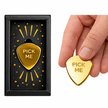 Gold-plated guitar pick charm with “Pick Me” engraving, held between fingers.