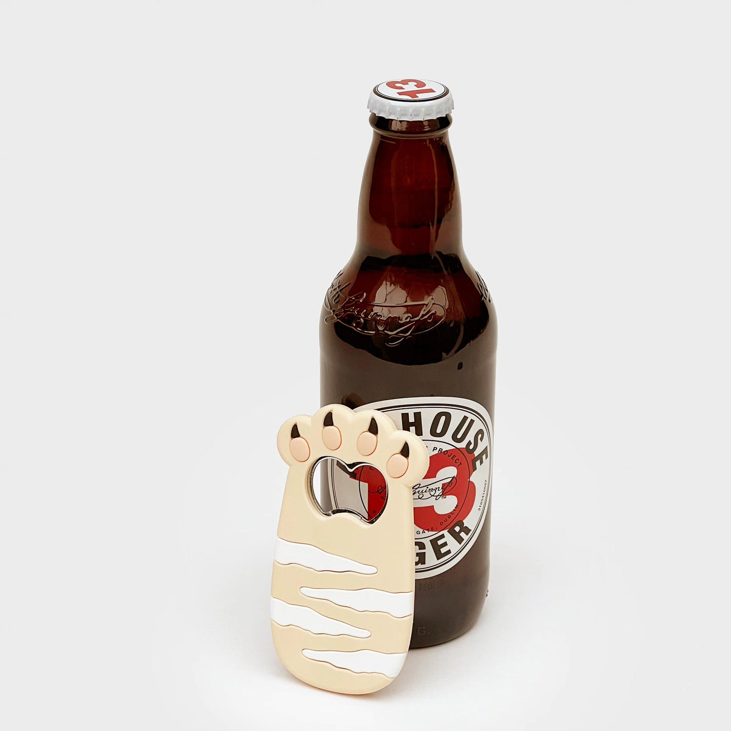 Cat-shaped bottle opener magnet beside a brown glass bottle with a silver cap.