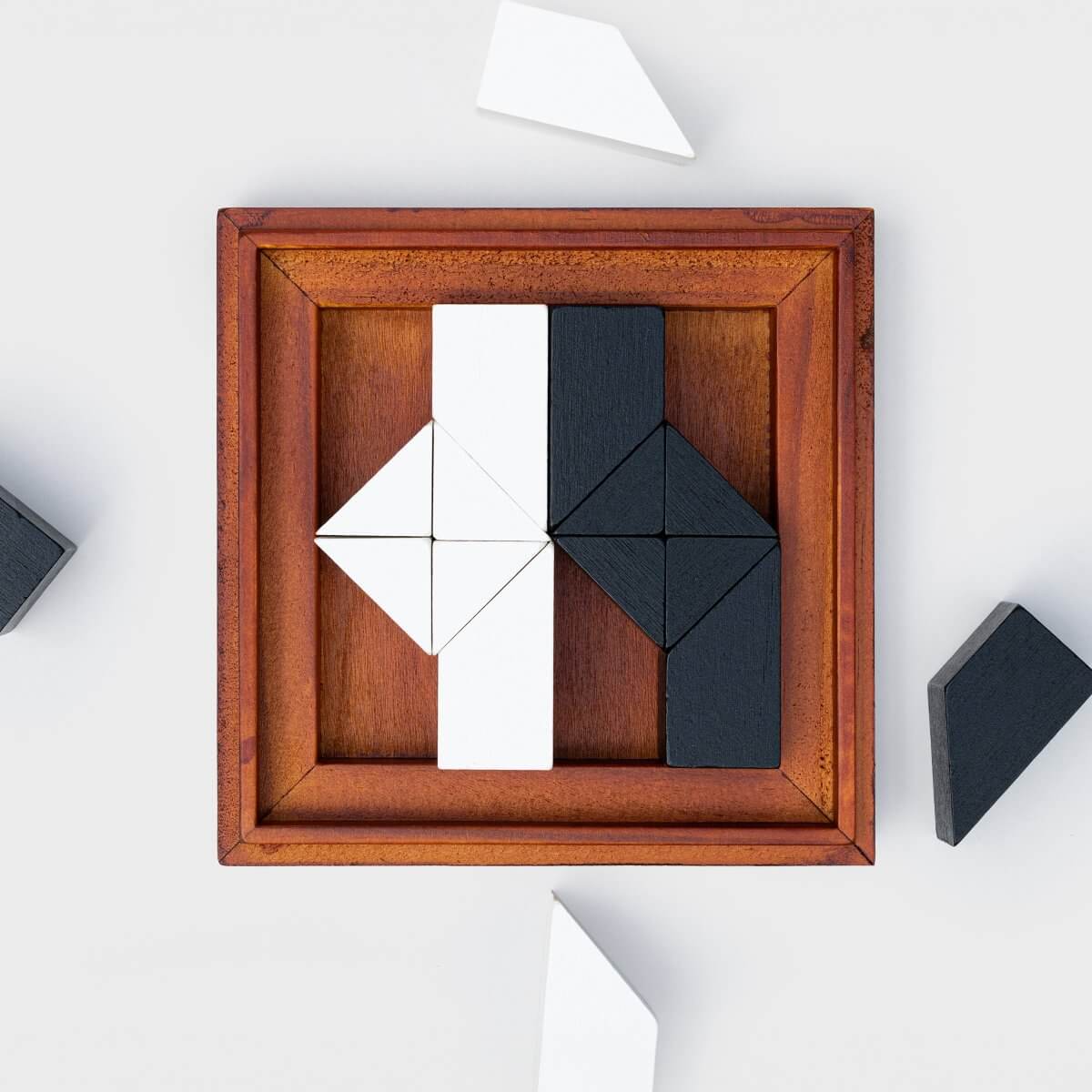 Wooden tangram puzzle in frame with white and dark interlocking tiles