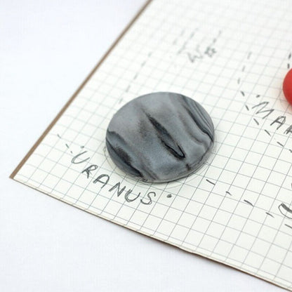 Planet-themed eraser, dark gray oval with black swirl on grid paper