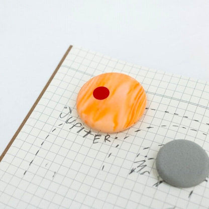 Orange planet eraser with a red dot and gray eraser nearby on grid paper