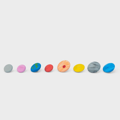 Row of eight planet-themed round erasers on a grid surface: gray, pink, blue, red, orange