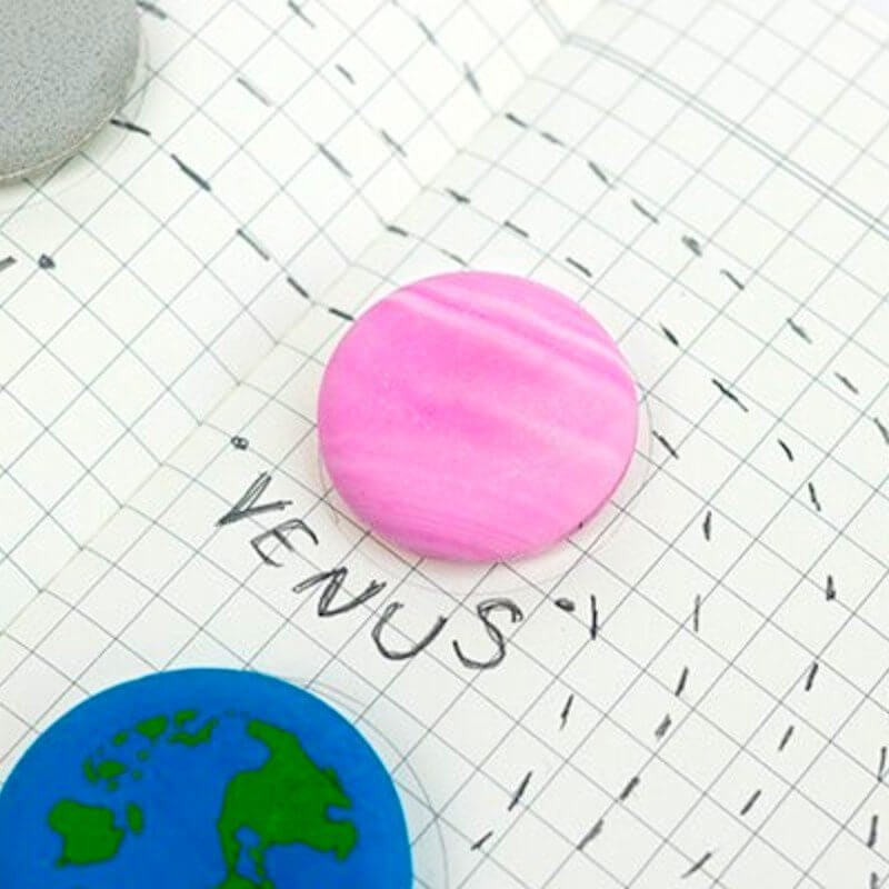 Pink round planet eraser on grid paper with blue Earth eraser partly visible