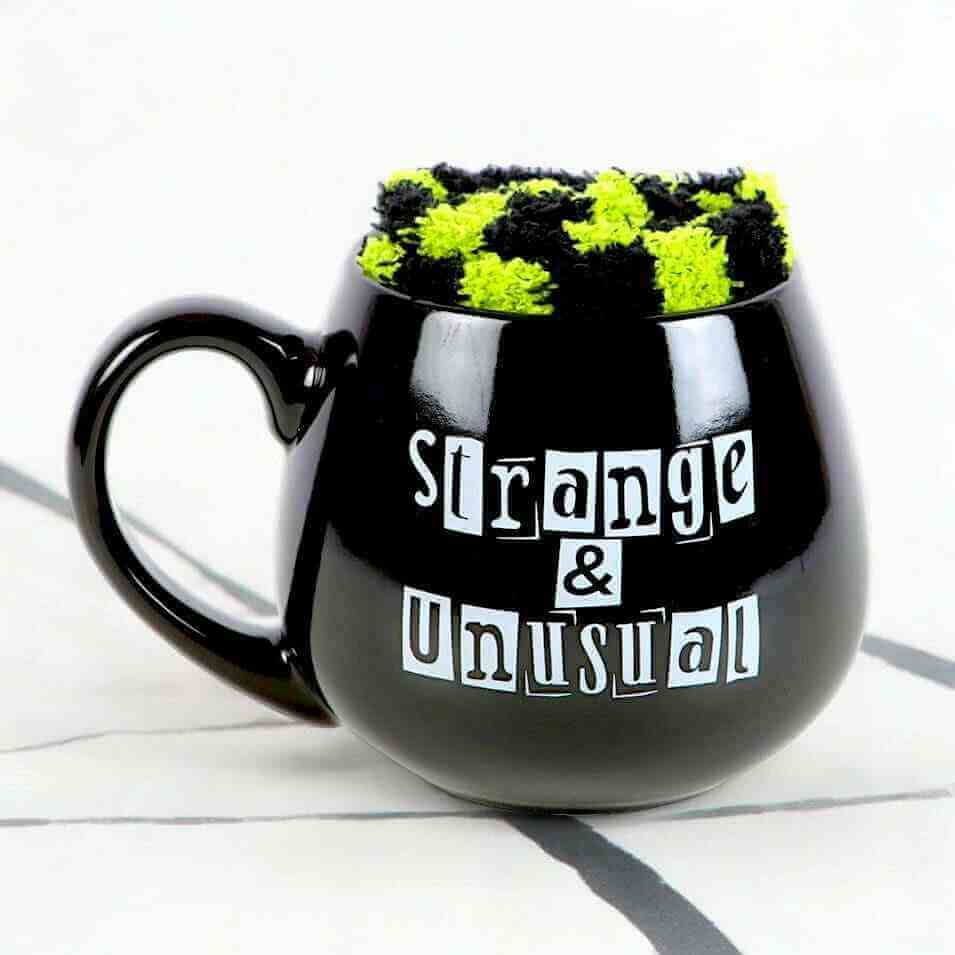 Black novelty mug with handle, 'Strange & Unusual' text, and green fuzzy top