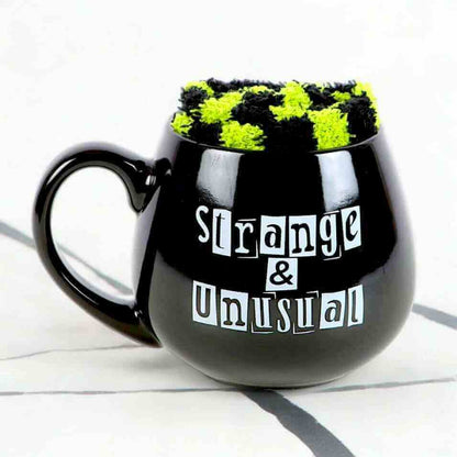 Black novelty mug with handle, 'Strange & Unusual' text, and green fuzzy top
