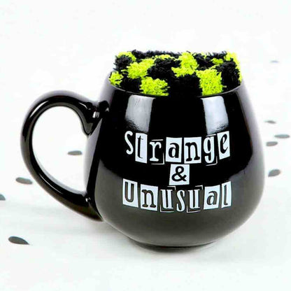 Black novelty mug with green fuzzy top and 'Strange & Unusual' slogan