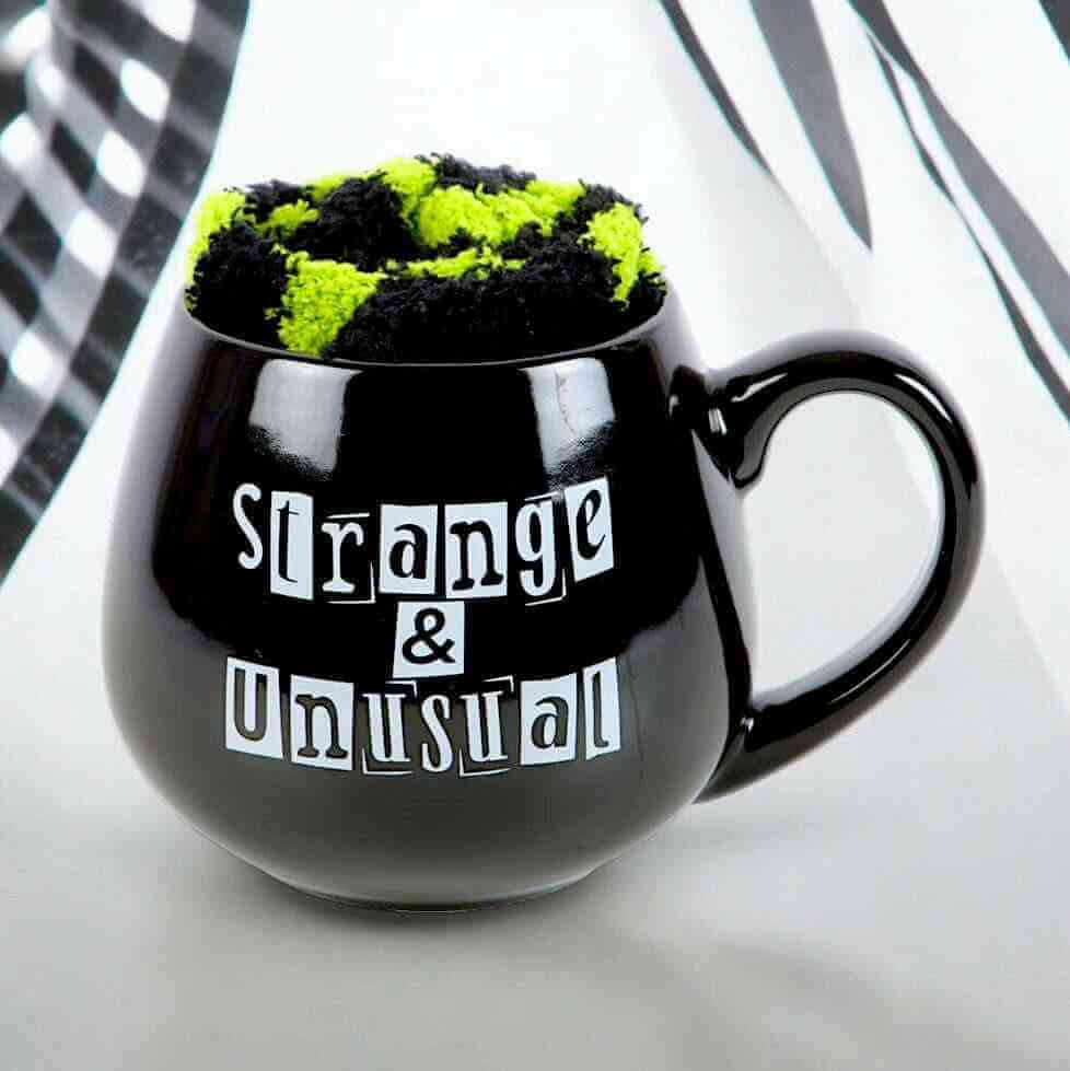 Black novelty mug with green-and-black fuzzy lid and 'Strange & Unusual' print