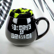 Black novelty mug with green-and-black fuzzy lid and 'Strange & Unusual' print